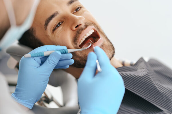 Smiling,Young,Man,Sitting,In,Dentist,Chair,While,Doctor,Examining
